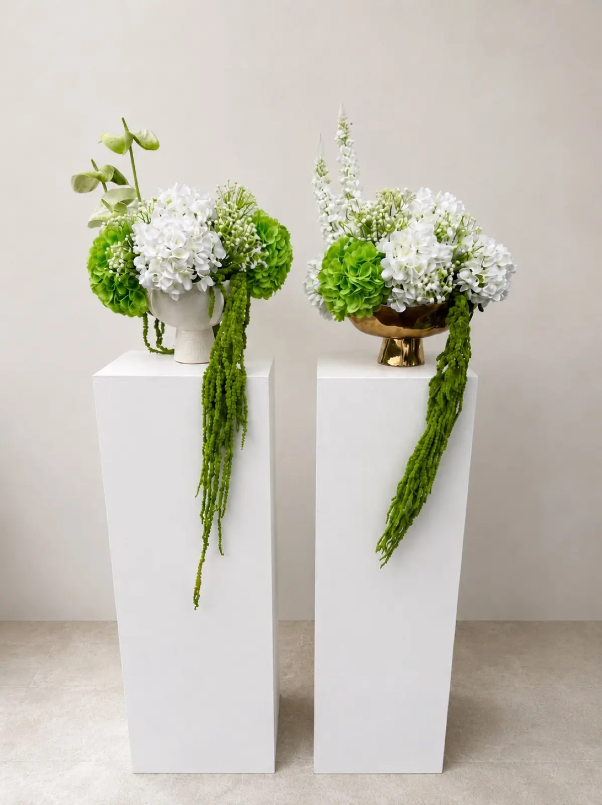 A lush faux floral centrepiece arrangement featuring white and green blooms with cascading trailing stems. Available in a white ceramic or gold bowl vase. Colours can be customized to suit your palette — perfect for wedding ceremony displays, reception tables, bridal showers, and elegant event styling. Pairs beautifully with our white display plinths.