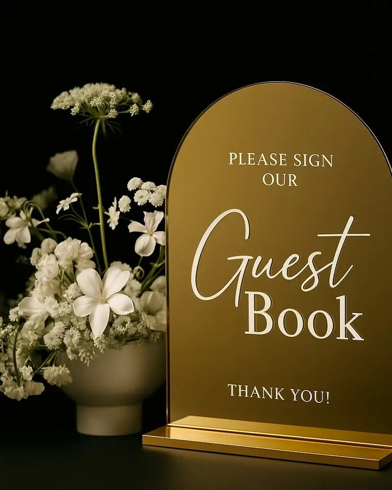 Elegant gold-finished acrylic arch sign reading 'Guestbook.' Coordinates with our table numbers and other acrylic signage for a unified aesthetic. Freestanding design pairs beautifully with our display plinths and card boxes.