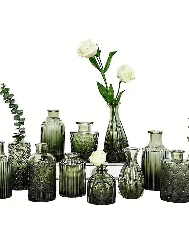 A box of 12 mini green glass bud vases, each holding a single stem or small sprig of greenery. Scatter across guest tables, along windowsills, or on the head table for a fresh, garden-inspired look. The green glass catches light beautifully.